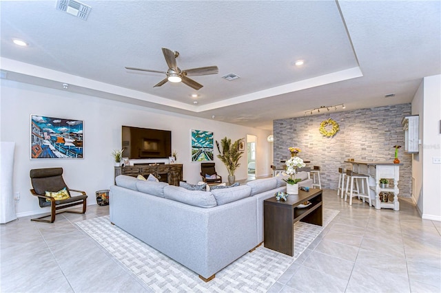 living room featuring a tray ceiling, ceiling fan, light tile patterned floors, and a textured ceiling