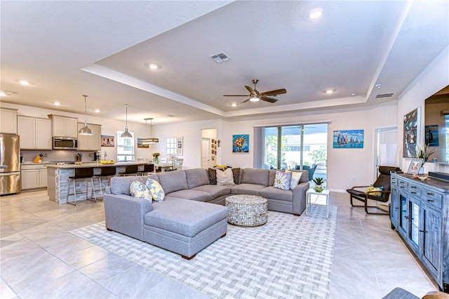 living room with a tray ceiling, ceiling fan, and light tile patterned flooring