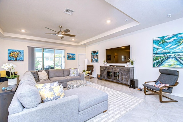 living room with ceiling fan, a raised ceiling, and light tile patterned floors