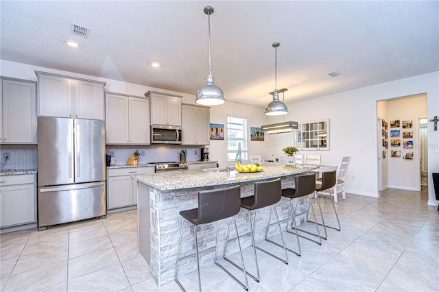 kitchen with light stone countertops, a kitchen bar, gray cabinetry, stainless steel appliances, and an island with sink