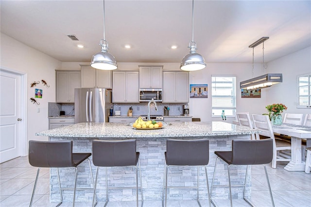 kitchen featuring decorative backsplash, gray cabinets, light stone countertops, and appliances with stainless steel finishes