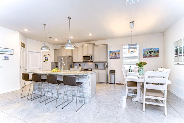 kitchen with hanging light fixtures, backsplash, stainless steel appliances, and a kitchen island with sink