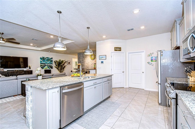 kitchen with ceiling fan, sink, hanging light fixtures, stainless steel appliances, and an island with sink