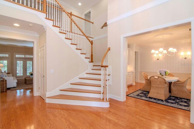 staircase featuring hardwood / wood-style flooring, french doors, crown molding, and a chandelier