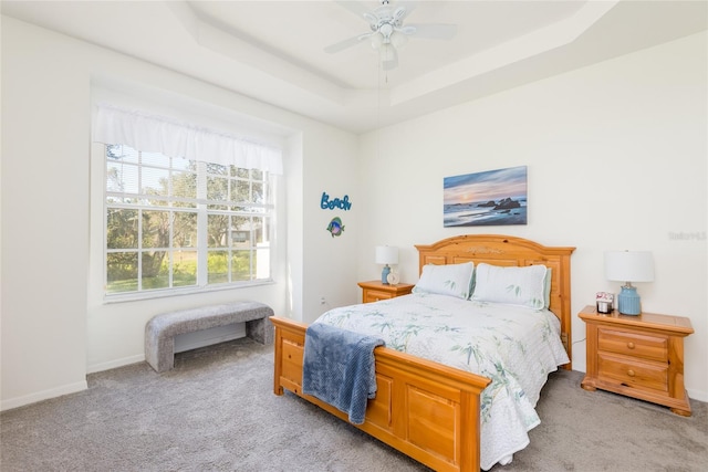 carpeted bedroom featuring ceiling fan and a tray ceiling