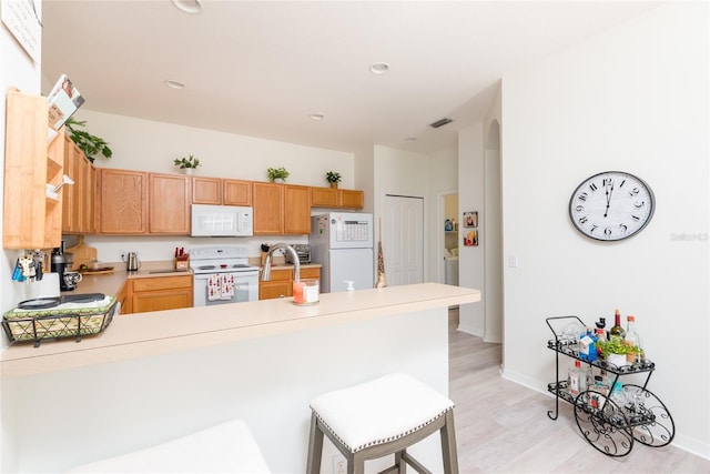 kitchen with a kitchen bar, light wood-type flooring, white appliances, and kitchen peninsula