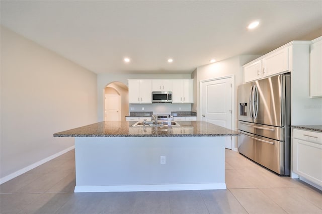 kitchen featuring dark stone counters, sink, an island with sink, and stainless steel appliances