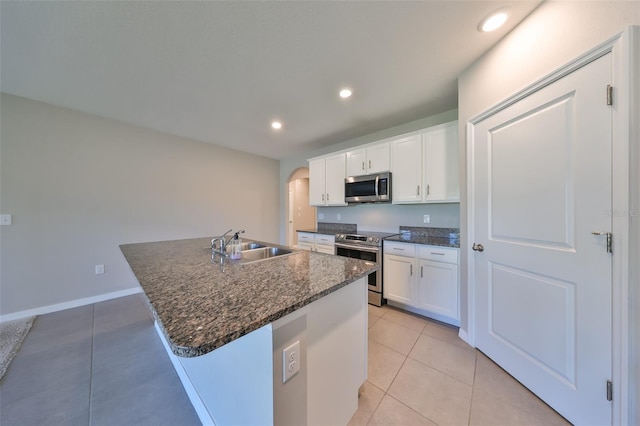 kitchen featuring stainless steel appliances, sink, light tile patterned floors, white cabinets, and an island with sink