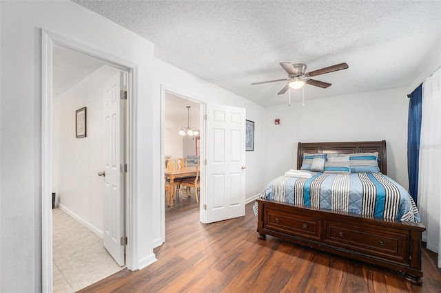 bedroom with a textured ceiling, ceiling fan with notable chandelier, and hardwood / wood-style flooring