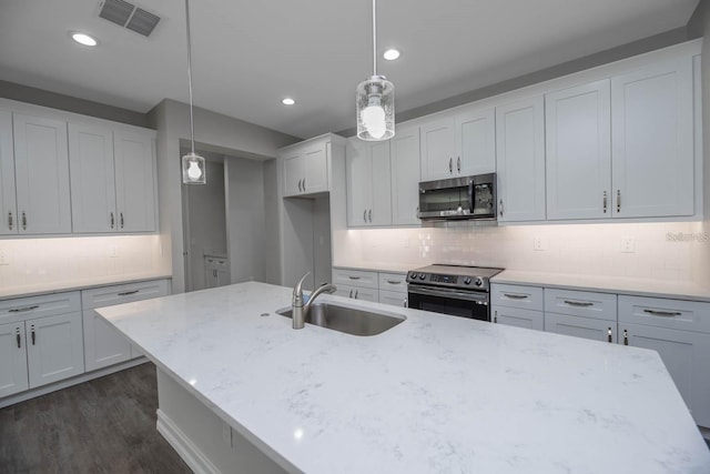 kitchen with appliances with stainless steel finishes, light stone counters, sink, pendant lighting, and dark hardwood / wood-style floors