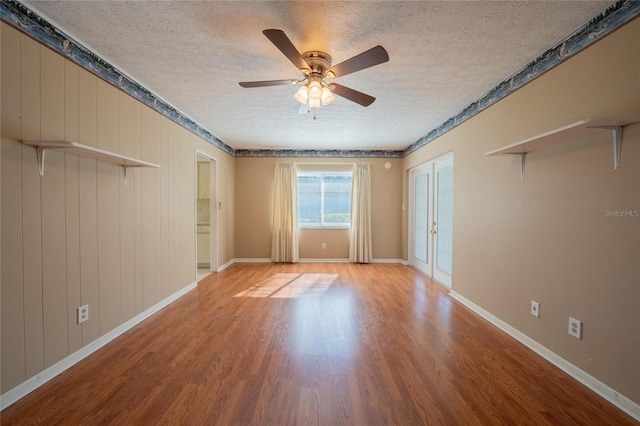 empty room featuring a textured ceiling, light wood-type flooring, ceiling fan, and wood walls