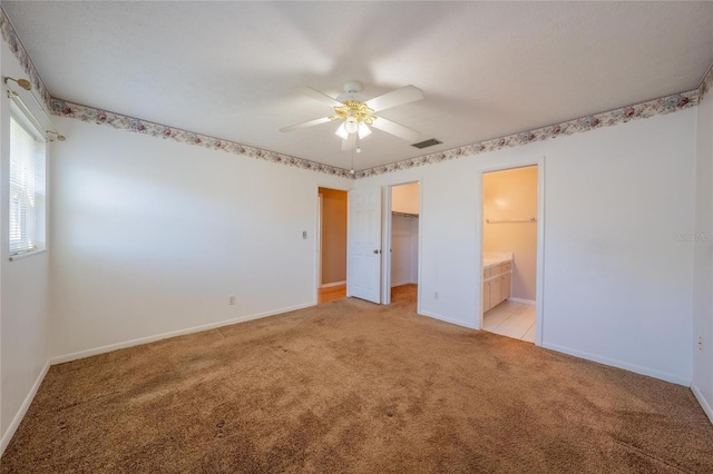 unfurnished bedroom with ceiling fan, ensuite bathroom, a walk in closet, light carpet, and a closet