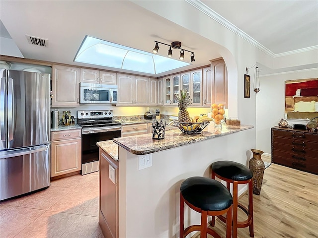 kitchen with a kitchen bar, kitchen peninsula, light stone countertops, stainless steel appliances, and light tile patterned floors