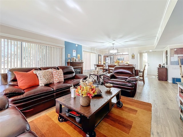 living room with crown molding, a chandelier, and light wood-type flooring