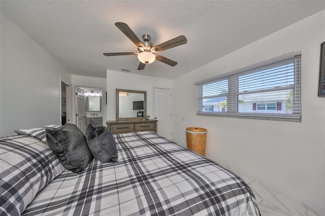 bedroom with ceiling fan, a textured ceiling, and connected bathroom