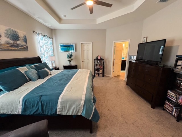 carpeted bedroom featuring a raised ceiling, connected bathroom, and ceiling fan