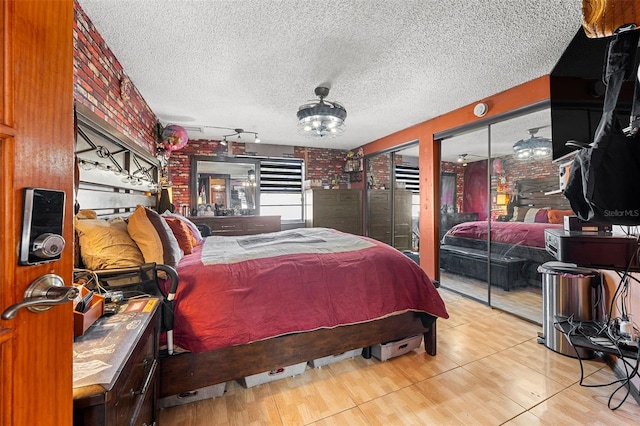 bedroom featuring light wood-type flooring, a textured ceiling, and brick wall