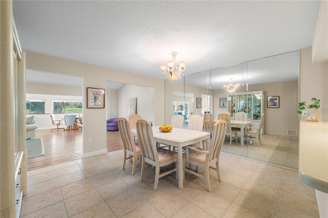 dining space with light wood-type flooring, a textured ceiling, and a chandelier