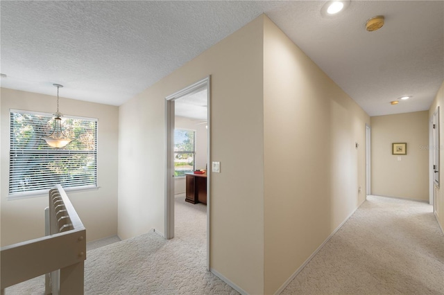 corridor with light colored carpet and a textured ceiling