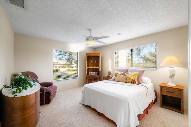 bedroom featuring a textured ceiling, light colored carpet, and ceiling fan