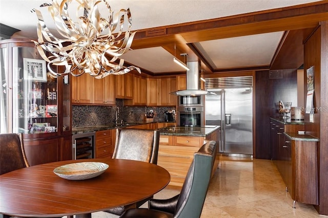 kitchen with island exhaust hood, decorative backsplash, stainless steel built in fridge, beverage cooler, and a chandelier