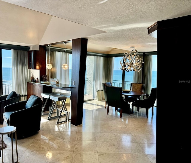 dining room with a chandelier, a textured ceiling, a water view, and a healthy amount of sunlight