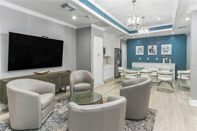 living room featuring ornamental molding, light hardwood / wood-style floors, a raised ceiling, and a notable chandelier