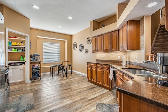 kitchen with dark stone counters, a textured ceiling, sink, light hardwood / wood-style flooring, and dishwasher