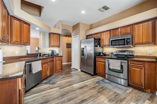 kitchen with appliances with stainless steel finishes, light hardwood / wood-style floors, tasteful backsplash, and dark stone counters