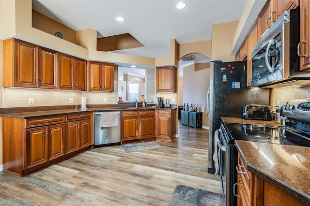 kitchen with backsplash, sink, dark stone countertops, appliances with stainless steel finishes, and light hardwood / wood-style floors