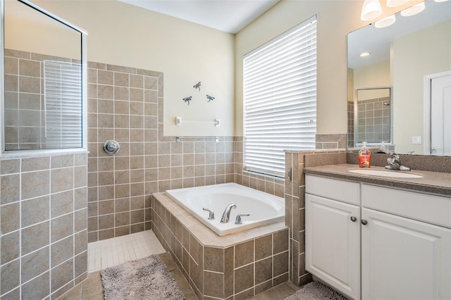 bathroom featuring tile patterned flooring, vanity, a relaxing tiled tub, and tile walls