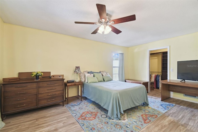 bedroom featuring ceiling fan, light hardwood / wood-style flooring, a textured ceiling, a walk in closet, and a closet