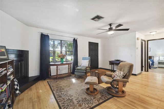 living area with ceiling fan, a textured ceiling, and light wood-type flooring