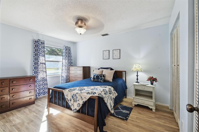 bedroom with light wood-type flooring, a textured ceiling, a closet, and ceiling fan