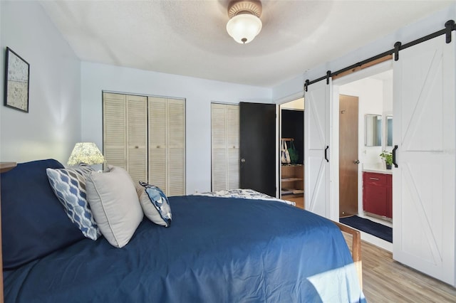 bedroom with ensuite bath, light hardwood / wood-style flooring, a textured ceiling, multiple closets, and a barn door