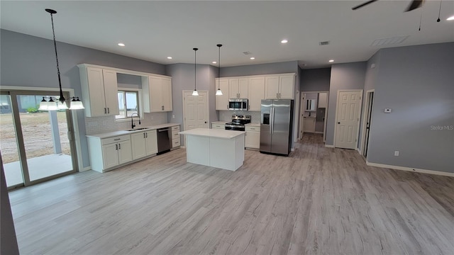 kitchen with appliances with stainless steel finishes, sink, decorative light fixtures, a center island, and white cabinetry