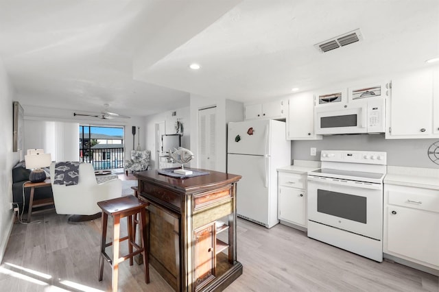 kitchen featuring white appliances, white cabinets, ceiling fan, light wood-type flooring, and a kitchen bar