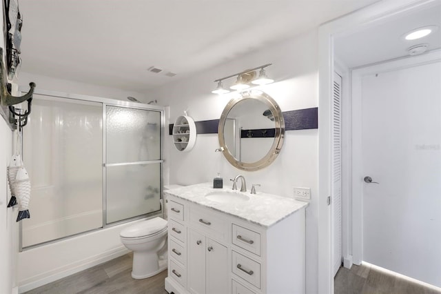 full bathroom with shower / bath combination with glass door, hardwood / wood-style floors, vanity, and toilet