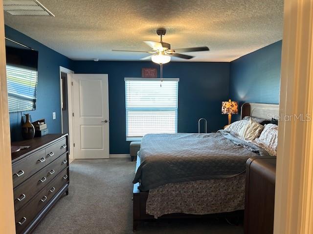 bedroom with ceiling fan, carpet floors, and a textured ceiling