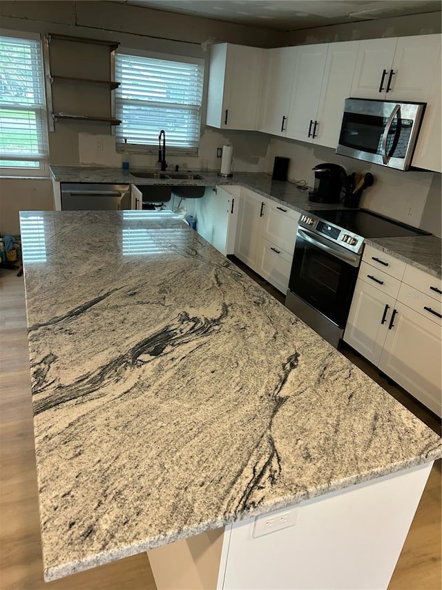 kitchen with appliances with stainless steel finishes, light stone counters, wood-type flooring, a center island, and white cabinetry