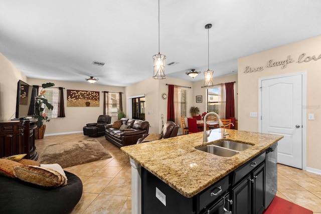 kitchen with a center island with sink, sink, light stone countertops, light tile patterned floors, and decorative light fixtures