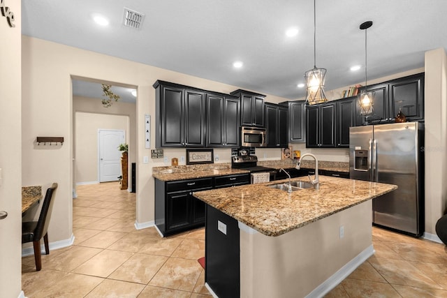 kitchen with light stone countertops, sink, stainless steel appliances, an island with sink, and pendant lighting