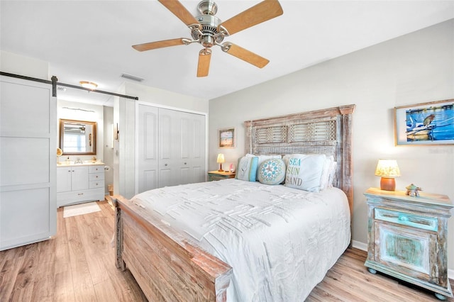 bedroom with ceiling fan, a barn door, light hardwood / wood-style floors, and a closet