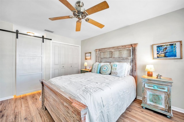 bedroom featuring ceiling fan, a barn door, light wood-type flooring, and a closet