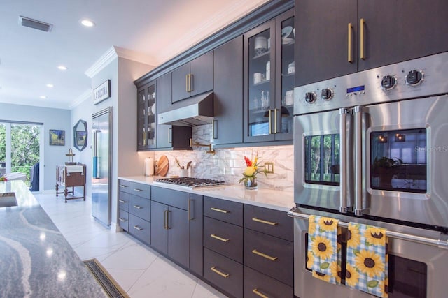 kitchen with appliances with stainless steel finishes, backsplash, light stone counters, dark brown cabinets, and crown molding