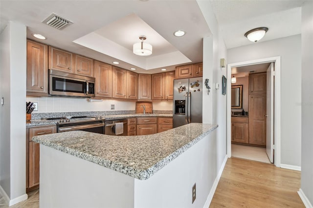 kitchen featuring light stone countertops, stainless steel appliances, light hardwood / wood-style floors, a tray ceiling, and decorative backsplash