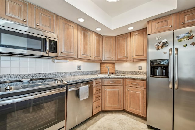 kitchen with tasteful backsplash, light stone counters, sink, and appliances with stainless steel finishes