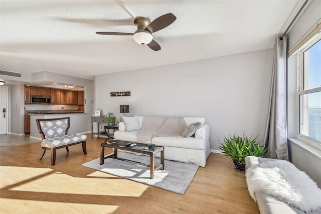 living room with ceiling fan, a textured ceiling, and light wood-type flooring