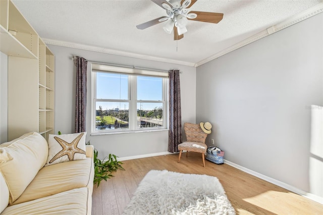 sitting room featuring ceiling fan, light wood-type flooring, a textured ceiling, and ornamental molding