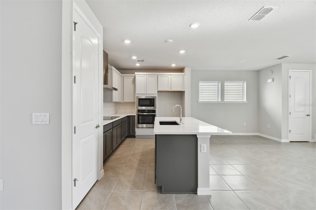 kitchen with sink, light tile patterned floors, appliances with stainless steel finishes, an island with sink, and white cabinets